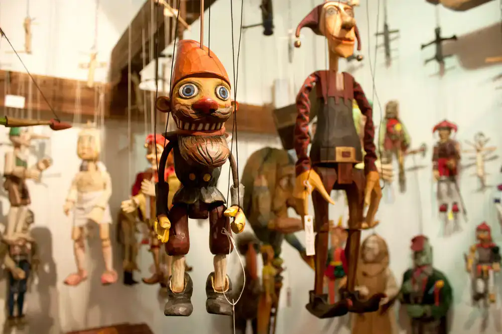 A craftsman holding a completed wooden marionette in the workshop